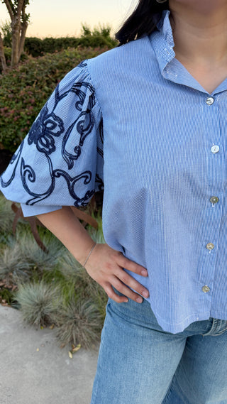 Woman wearing a button up in light blue shirt with patterned sleeves.