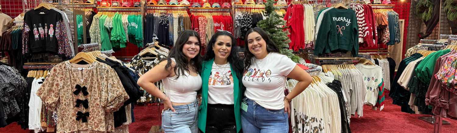 Three women posing in a clothing store with racks of clothes and Christmas decorations in the background.
