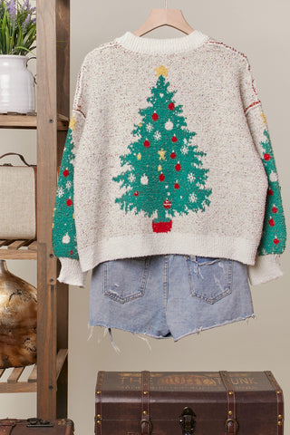 Sweater with Christmas tree design on a hanger against a neutral background