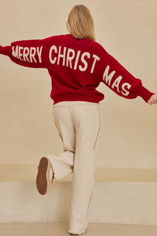 Person wearing a red sweater with 'MERRY CHRISTMAS' text, standing against a beige wall.